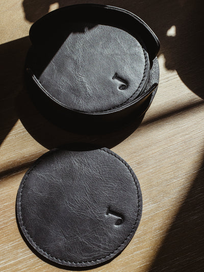 Circular black leather coaster set on wood table.