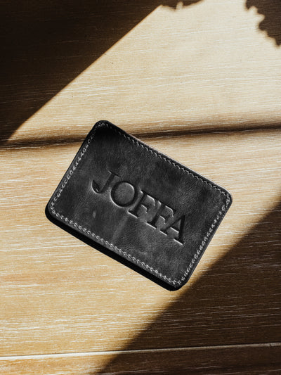 Black minimalistic wallet with large logo on back. Product is on a wood surface.
