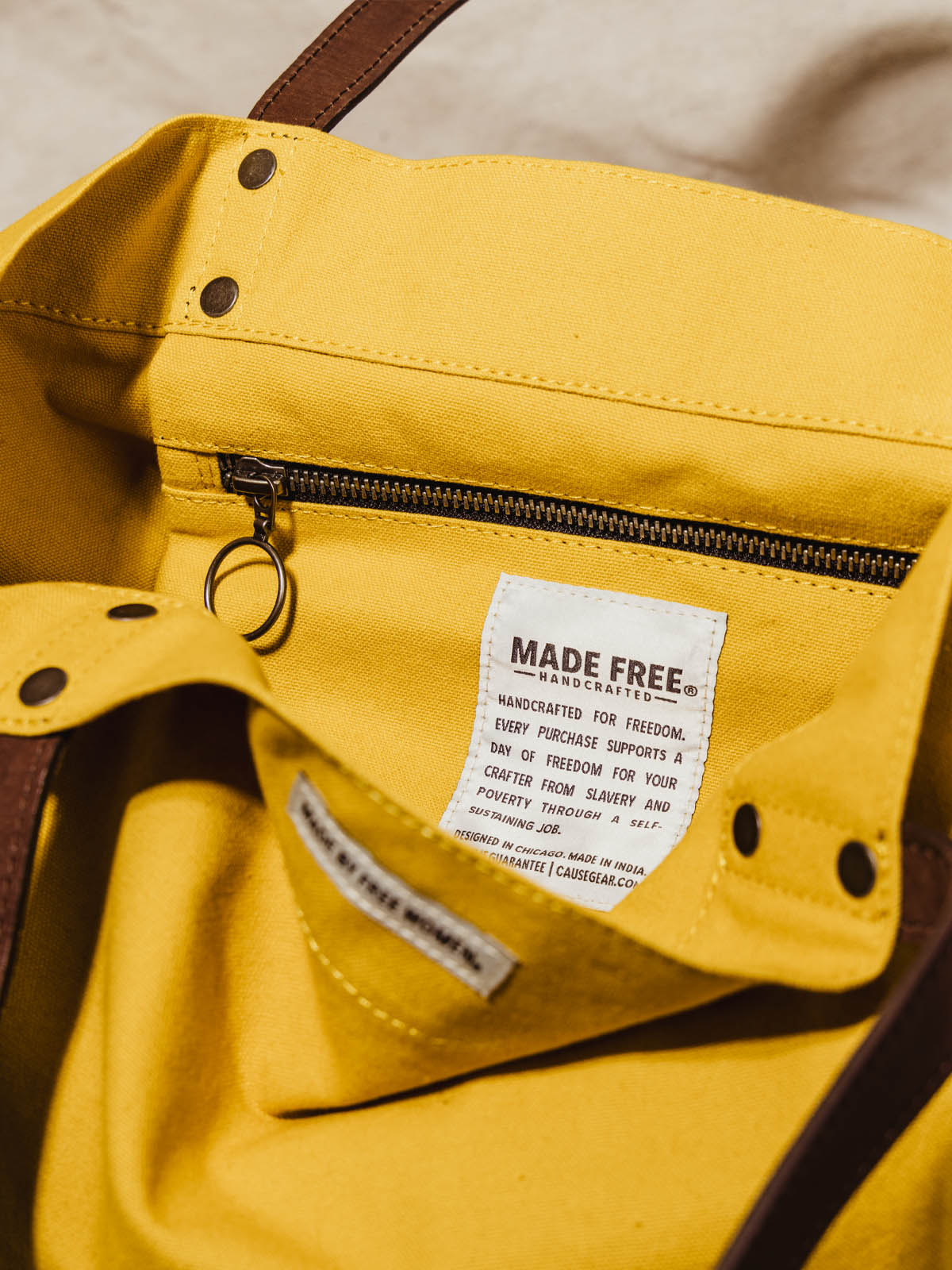 Interior zipper and table of made free yellow tote bag with leather straps on canvas cloth bag ground with dry plants.