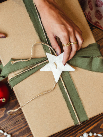Hand adjusting white star decoration on eco-friendly Christmas present wrapped with green ribbon and twine on rustic wooden floor.