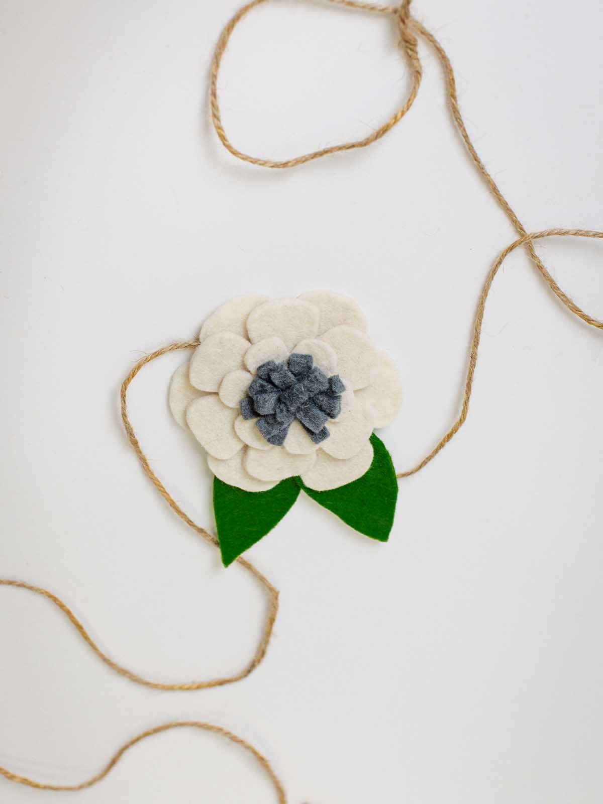 Handmade felt flower ornament with green leaves and natural jute twine, perfect for holiday gift wrapping or garland embellishment.