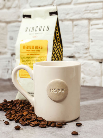 Handmade hope mug on kitchen counter with bag of coffee and spilt coffee beans.