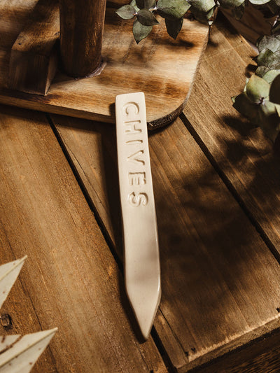 Ceramic garden marker "chives" lying on a wooden surface with some greenery. 