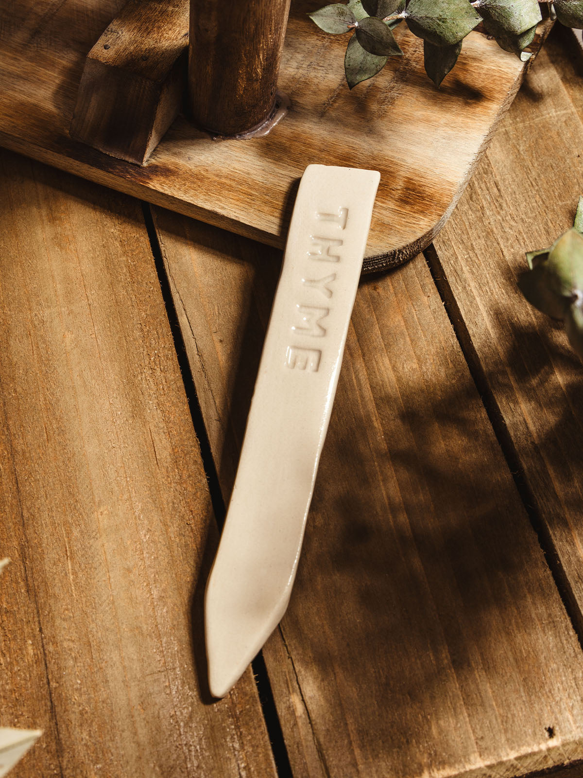 Ceramic garden marker "thyme" lying on a wooden surface with some greenery. 