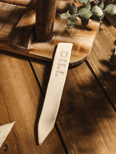 Ceramic garden marker "dill" lying on a wooden surface with some greenery. 