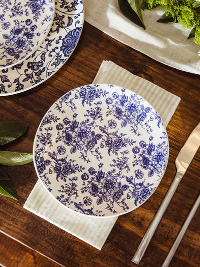 A blue and white floral salad plate set on a striped napkin with modern silver flatware, part of a refined and natural table setting.