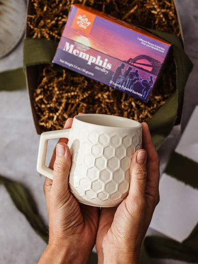 Hands holding honeycomb textured ceramic mug from Memphis gift bundle with Memphis Medley tea sampler, artisan tea and mug set packaged in eco-friendly gift box, unique Memphis-inspired present.