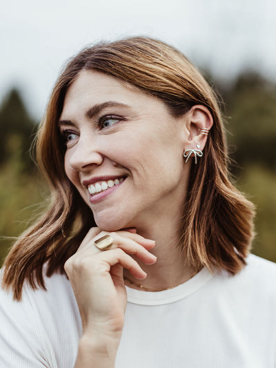 Woman wearing silver bow stud earrings and gold statement ring, ethical handmade jewelry styled with casual white top.
