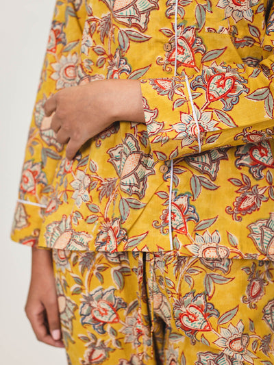 Close-up of the yellow floral pajama top and pants, showing the button details, white piping, and vibrant red, blue, and green floral patterns.