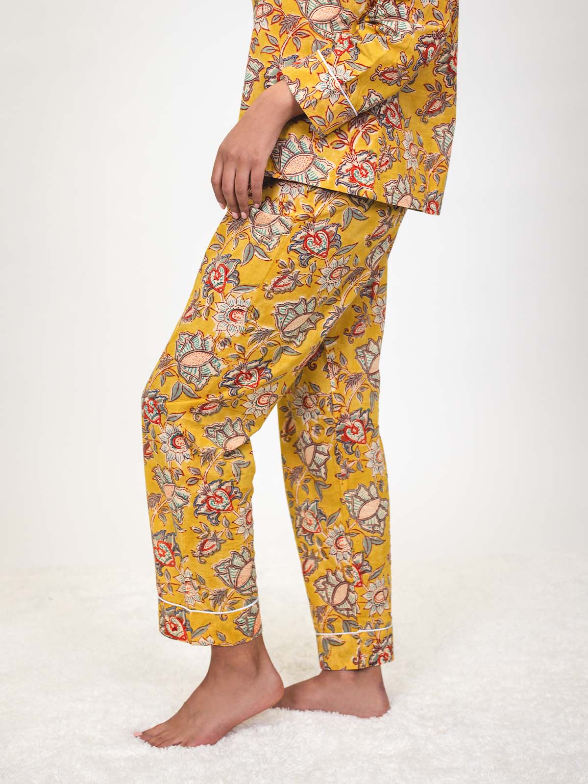 Side view of a woman wearing yellow floral pajamas, showing the straight-leg fit of the pants and white piping at the cuffs.