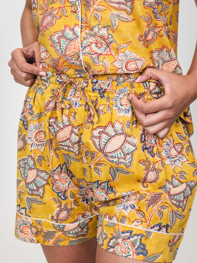 Close-up of a woman wearing yellow floral pajama shorts, holding the elastic waistband with both hands to show the drawstring detail.