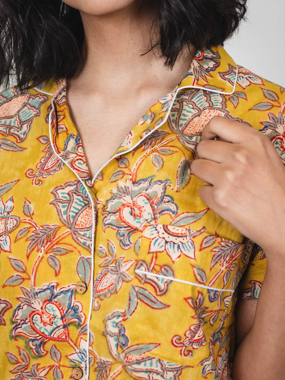 Close-up of the upper half of a yellow floral short-sleeve pajama top, showing white piping detail along the collar and pocket.