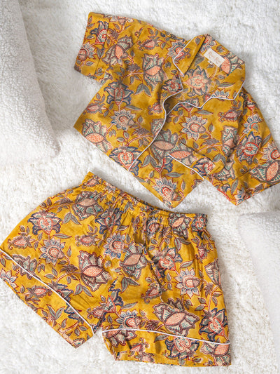  Folded yellow floral short-sleeve pajama set with matching shorts, displayed on a soft white textured surface between two white pillows.
