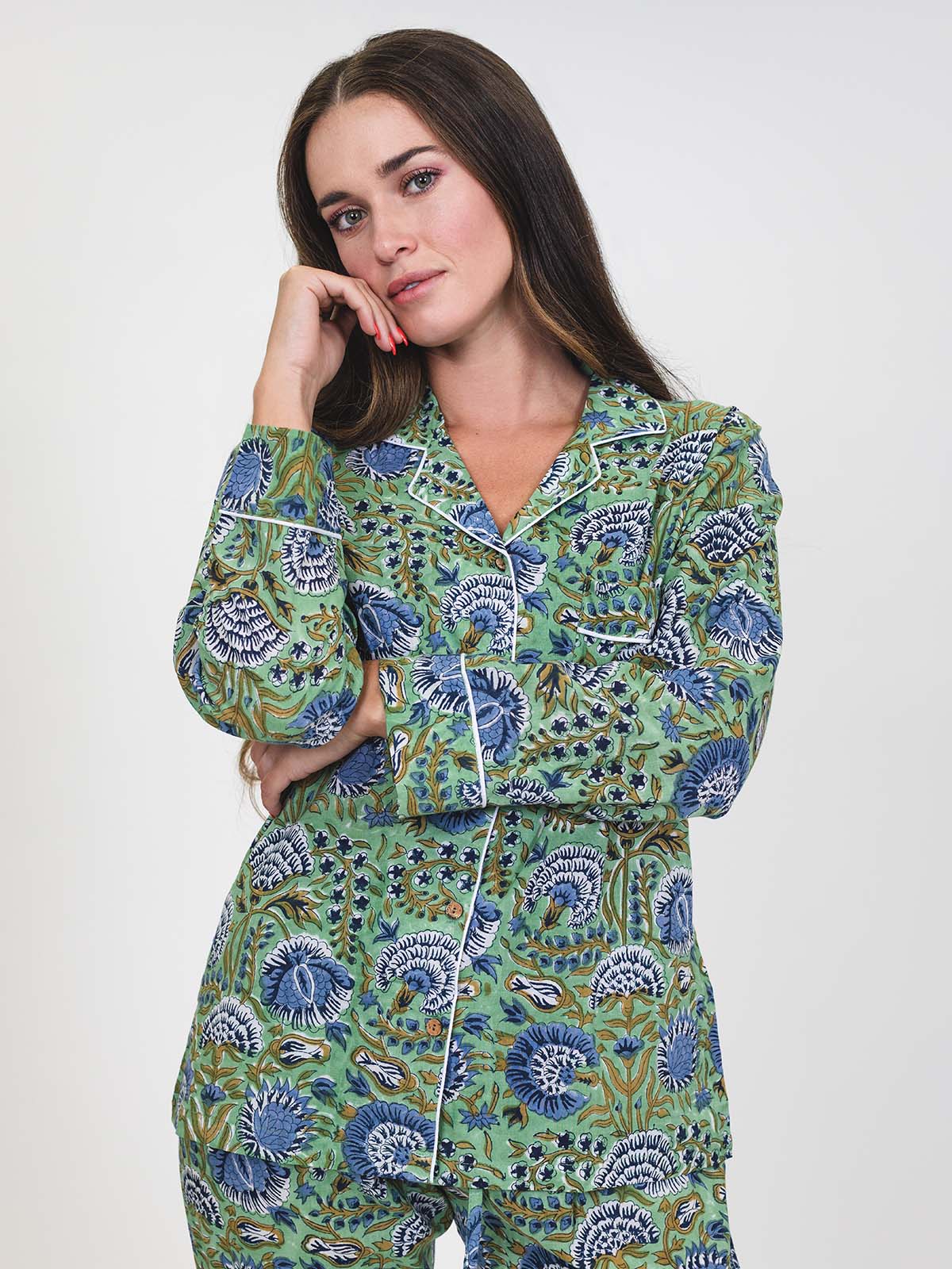 Close-up of a woman wearing a green pajama set with blue floral print and white piping, hand resting on her cheek, looking at the camera.