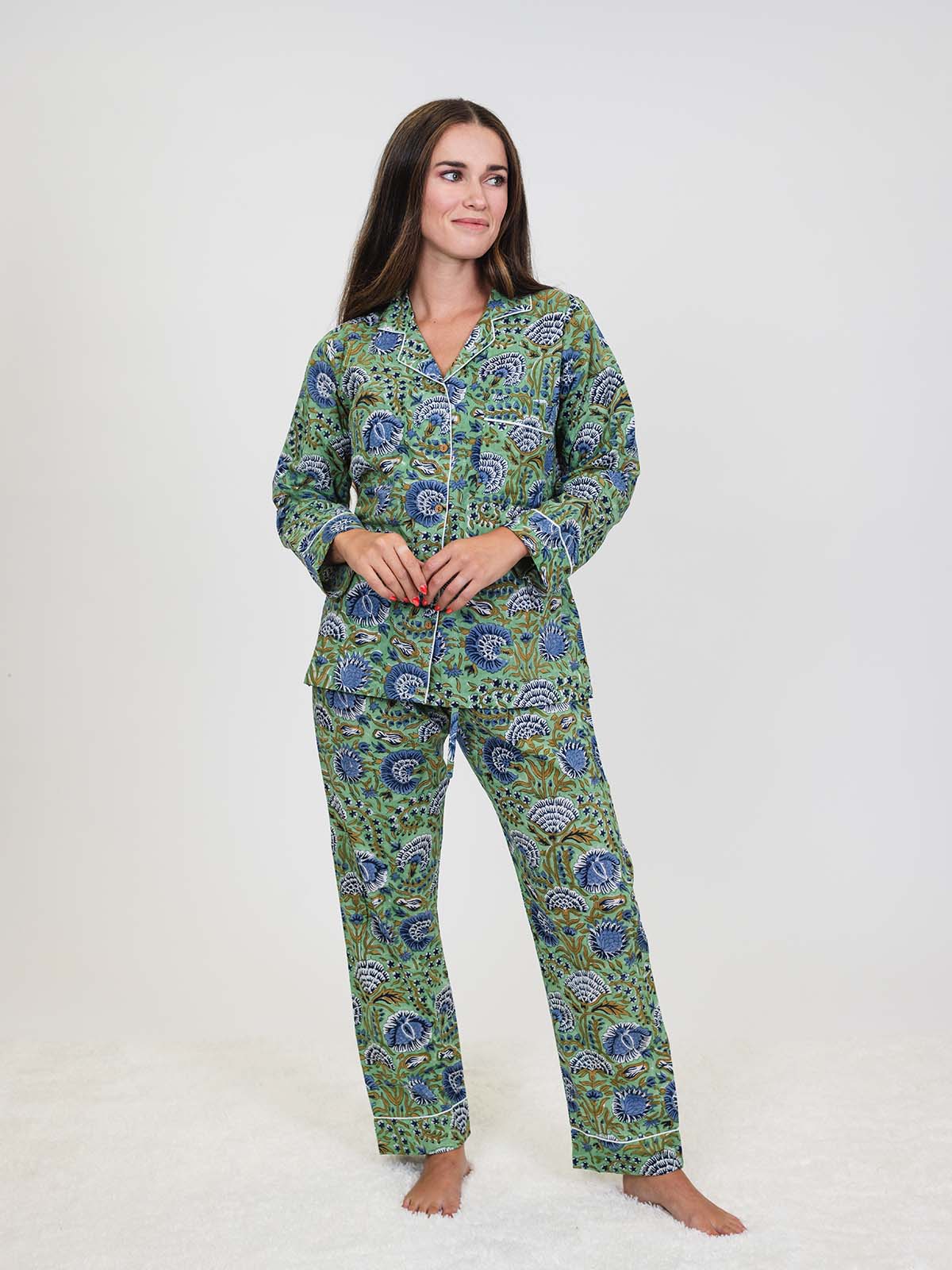 Woman standing in a green and blue floral pajama set with white piping, smiling slightly with hands clasped in front of her.