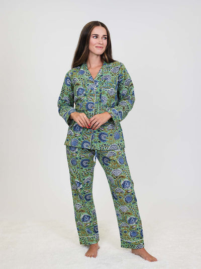 Woman standing in a green and blue floral pajama set with white piping, smiling slightly with hands clasped in front of her.