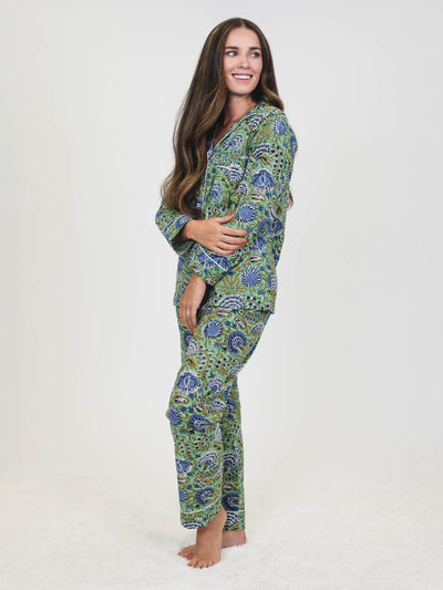 Side view of a woman in a green and blue floral pajama set with white piping, smiling and looking over her shoulder, with long hair draped over one side.