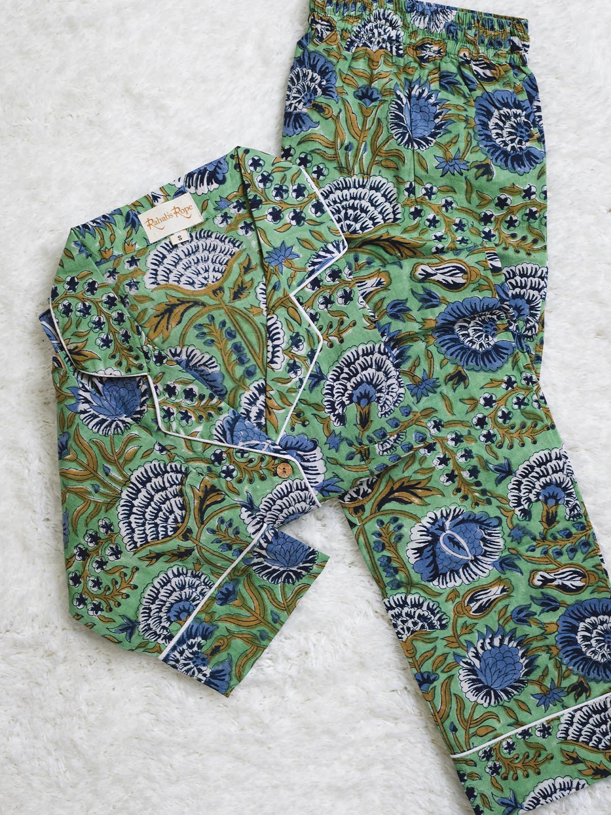 Folded green pajama set with blue and white floral print and white piping, displayed on a soft white textured surface.