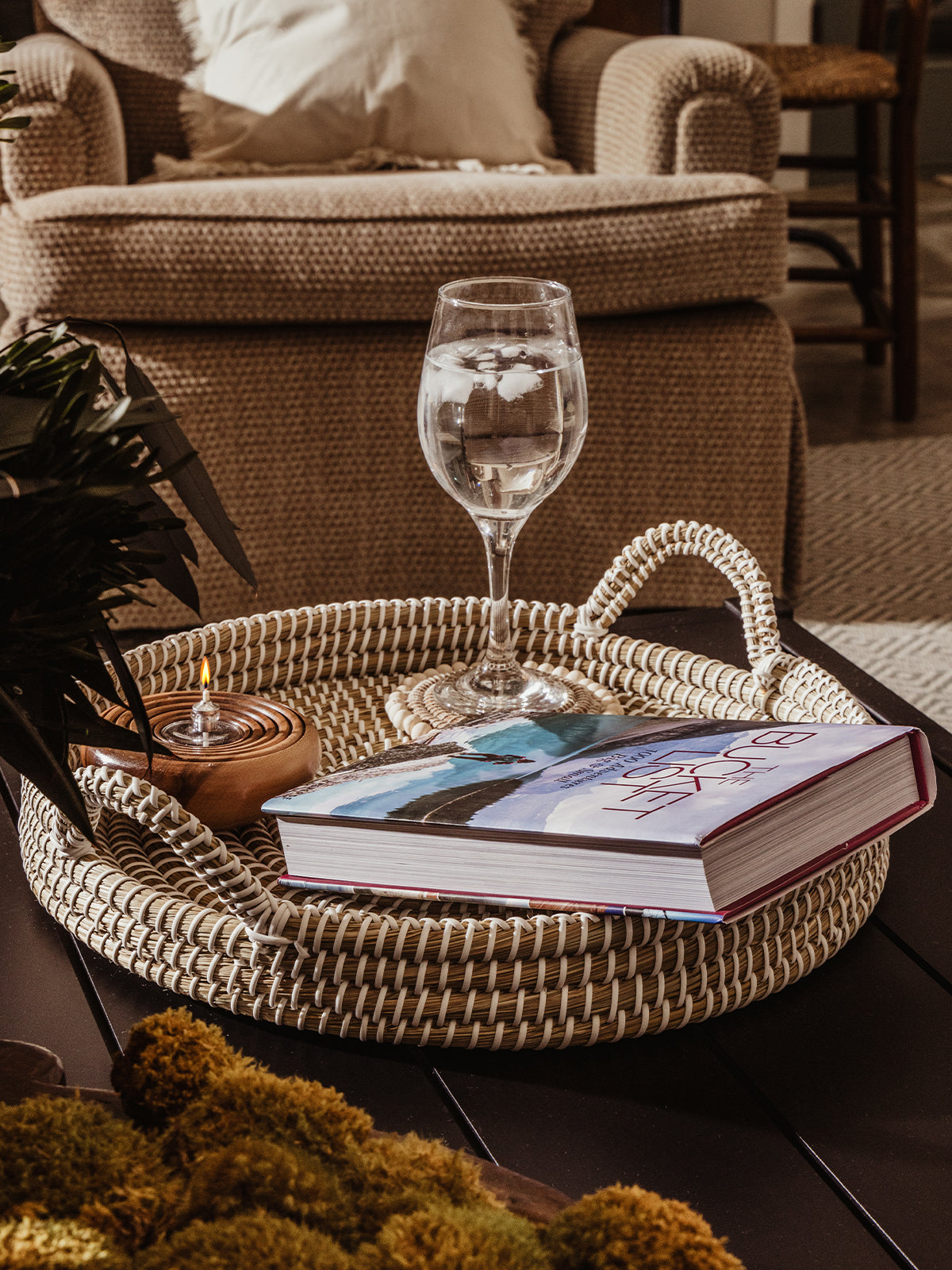 Kaisa tray with book, wine glass, and candle placed within. Tray is placed on a black coffee table in a living room space. 