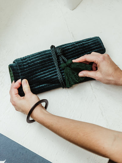 Hands wrapping a luxurious green velvet jewelry roll with tassel closure. Perfect for organizing and storing jewelry, ethically crafted by Rahab's Rope, available at Joffa.com.