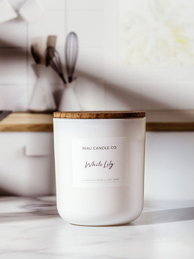 Riau Candle Co. White Lily soy wax candle with a wooden lid, styled on a kitchen counter with natural light and minimalist background.