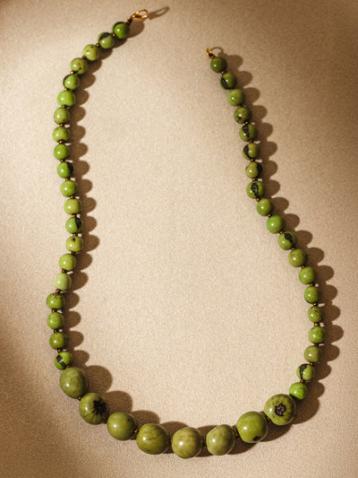 Flat lay of a handcrafted green beaded necklace with varying bead sizes and subtle marbling, arranged in a curve on a softly lit neutral background.