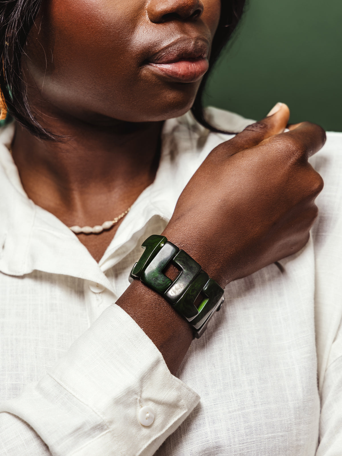 Portrait of a woman wearing a statement green link bracelet with a square cut-out design, styled with a white textured blouse and minimal jewelry.
