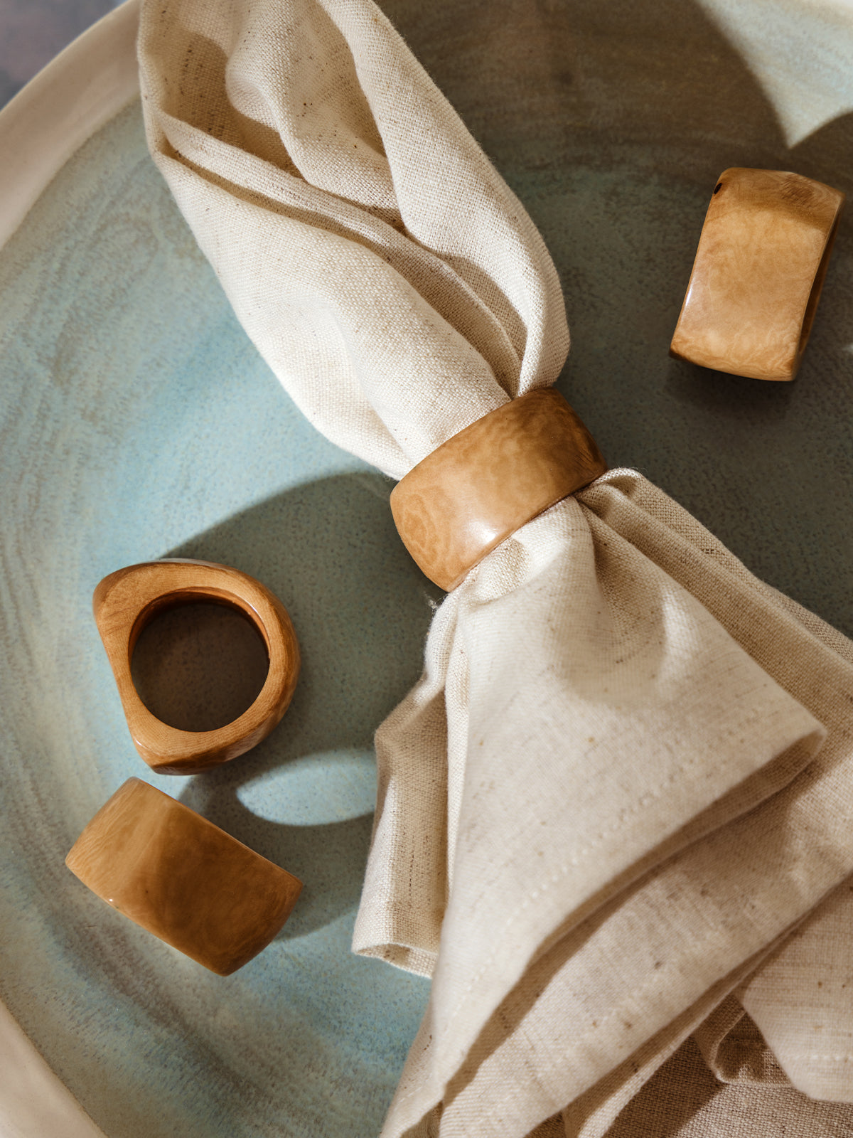 Handmade natural Tagua seed napkin rings in warm natural tan tones displayed on a soft blue-green ceramic plate, with a neutral linen napkin styled through one ring.