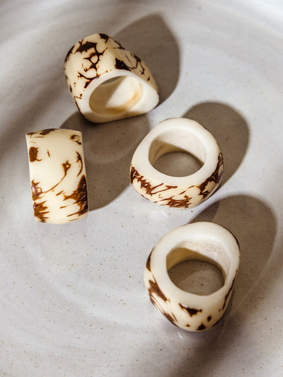 Close-up of four handmade Tagua seed napkin rings in creamy ivory with organic brown marbled patterns, displayed on a smooth, off-white ceramic plate.