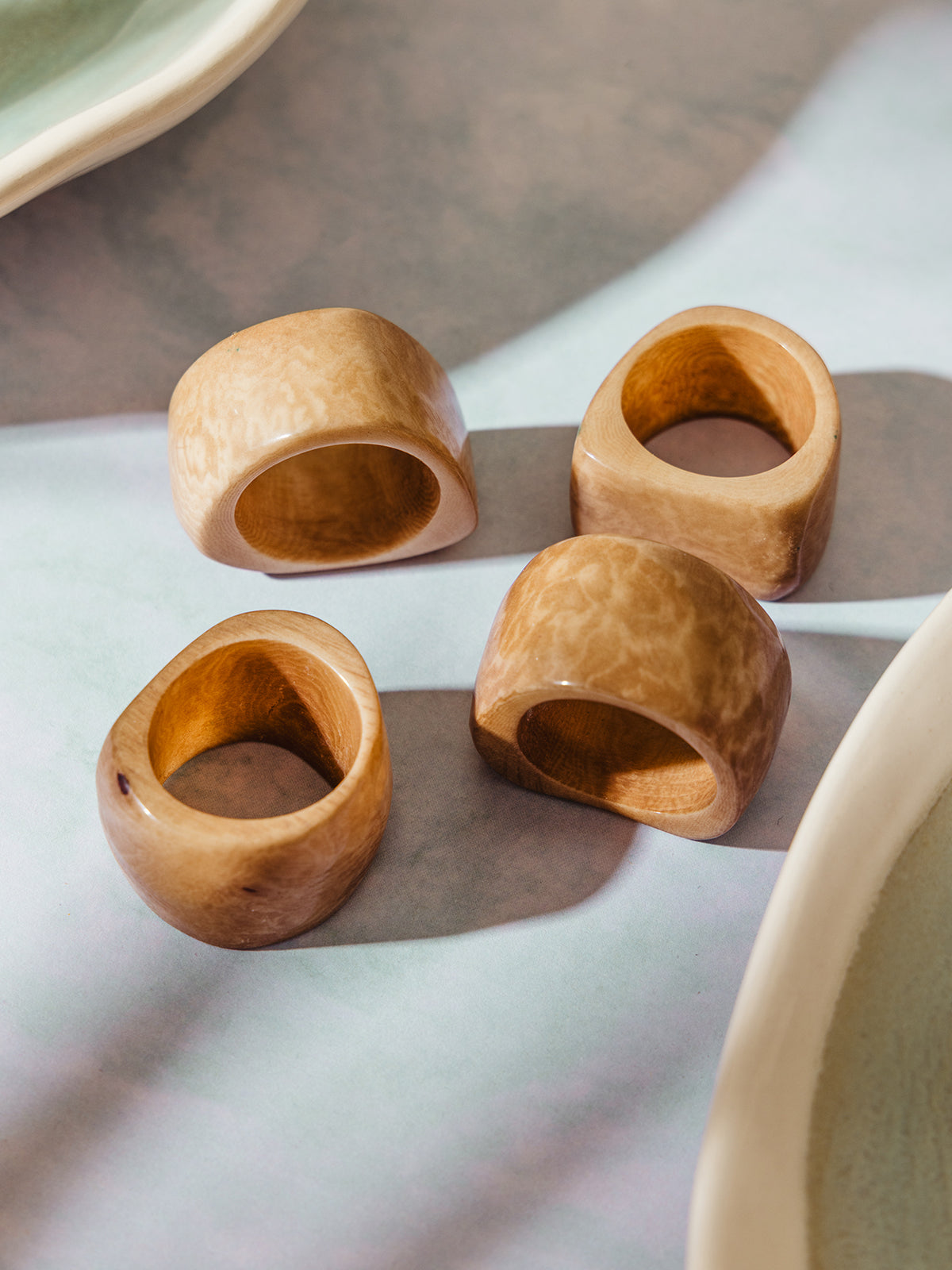 Set of four handmade Tagua seed napkin rings in polished natural tan, showcasing their organic grain and soft curves on a pastel-toned surface.