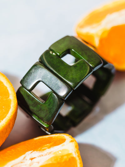 Close-up of a chunky green geometric link bracelet with a glossy finish, styled with halved oranges on a light pastel surface for a bold, fresh look.