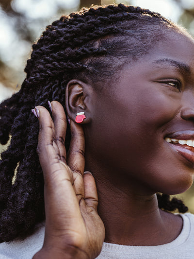 Side view close-up of handcrafted red and white stud earrings worn by a woman with braided hair, showcasing fair trade artisan jewelry.