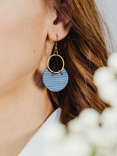 Close up of female wearing blue earring on golden hoop. 