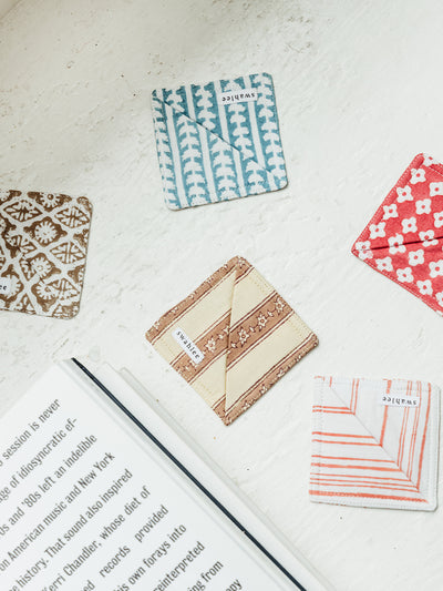 Handmade fabric bookmarks in blue and brown patterns, resting on an open book. Ethically crafted fabric bookmarks from Joffa.com, adding a stylish touch to reading accessories.