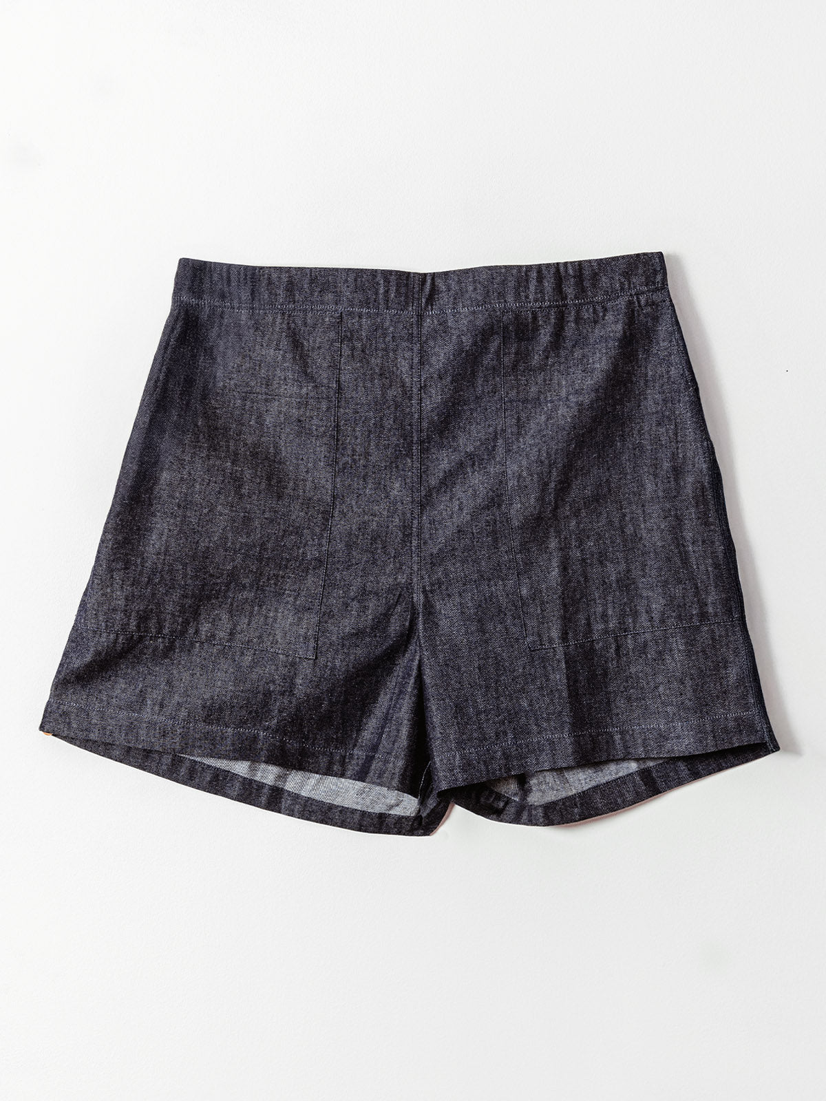 A pair of dark denim high-waisted shorts is laid flat against a light background. The shorts feature a clean, tailored front with subtle seam detailing and a slightly flared hem, offering a structured yet casual look.