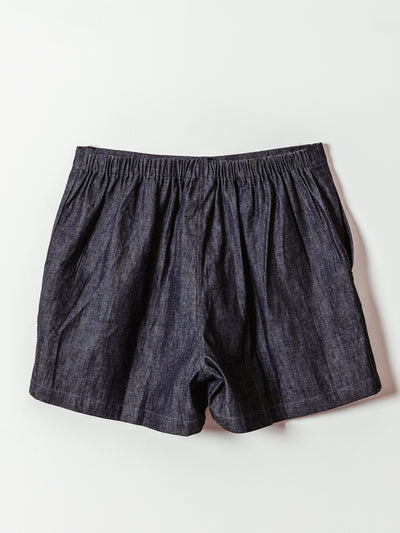 The back view of a pair of dark denim shorts laid flat against a light background. The shorts have an elastic waistband and gathered detailing, providing a relaxed and comfortable fit with a soft, easygoing silhouette.