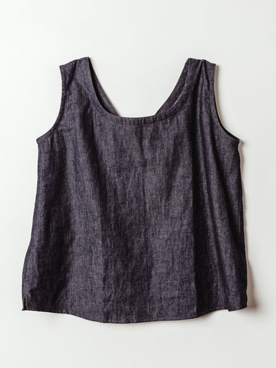 A dark denim tank top with wide straps is laid flat against a light background. The front features a scoop neckline and a minimal design, offering a simple and versatile silhouette.