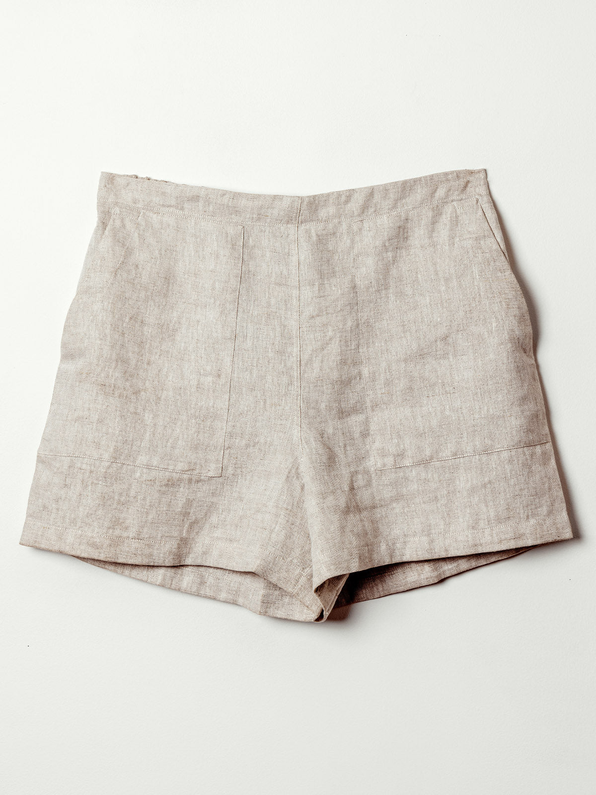 The front view of beige linen shorts displayed on a flat surface. The shorts have a smooth, tailored finish with front patch pockets and clean seam lines, combining comfort with structure.