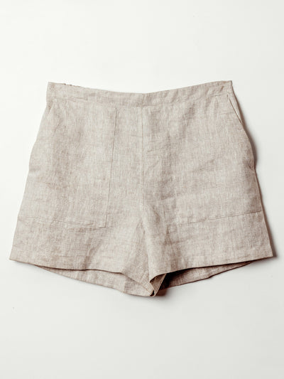 The front view of beige linen shorts displayed on a flat surface. The shorts have a smooth, tailored finish with front patch pockets and clean seam lines, combining comfort with structure.