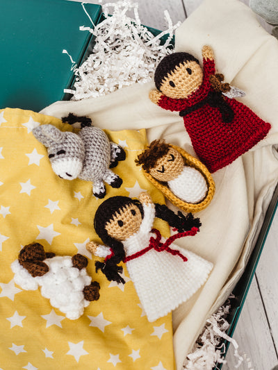 Handmade crochet Nativity finger puppets — Mary, Joseph, baby Jesus, donkey, and sheep — displayed in a gift box with yellow star cloth. Ethical fair trade Christmas gift idea for children.