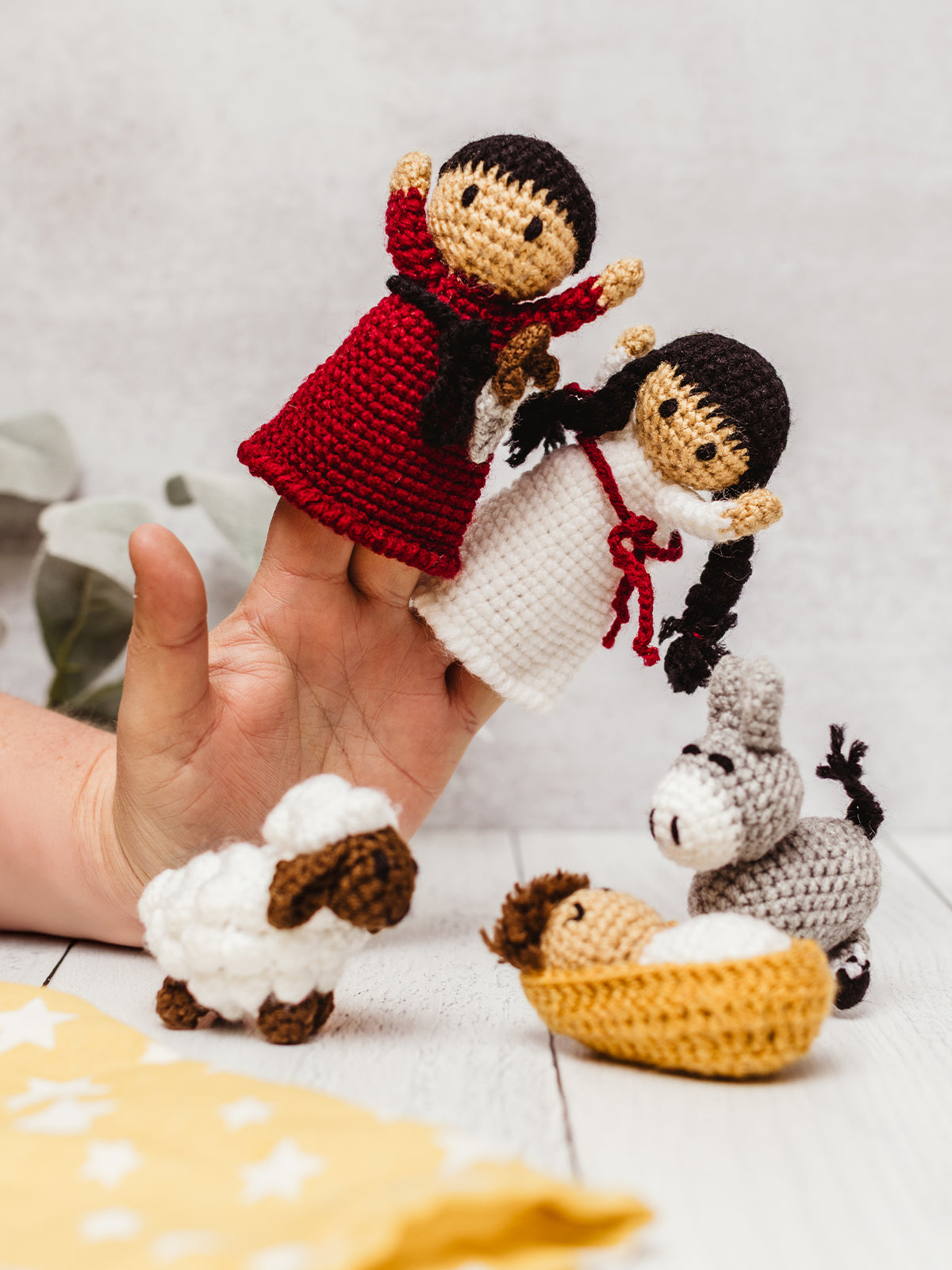 Hand holding handmade crochet Nativity finger puppets with Mary and Joseph, alongside a crocheted baby Jesus in a manger, sheep, and donkey. Ethical fair trade Christmas toy set for kids and holiday storytelling.