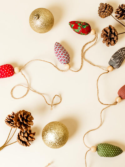 Festive Christmas garland featuring handmade fabric ornaments in red, green, and patterned designs, accented with wooden beads, displayed alongside glittery gold baubles and pinecones, part of Joffa.com's eco-friendly holiday decor collection.