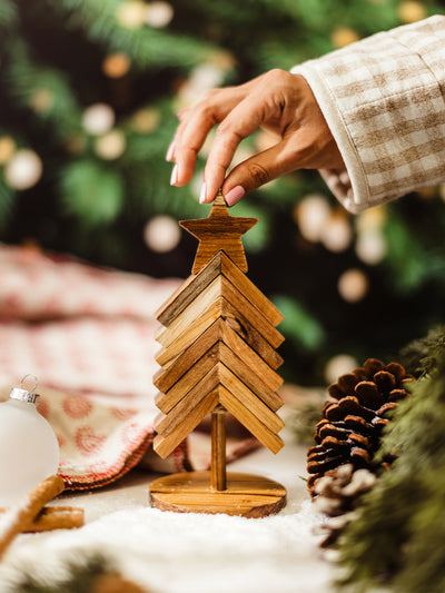 Hand placing a wooden star on top of a handcrafted wooden Christmas tree decoration, eco-friendly holiday décor with pinecones and festive greenery.