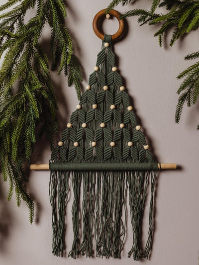 Handcrafted green macramé Christmas tree wall hanging with wooden beads, displayed against a neutral wall, surrounded by festive greenery for a natural holiday look.