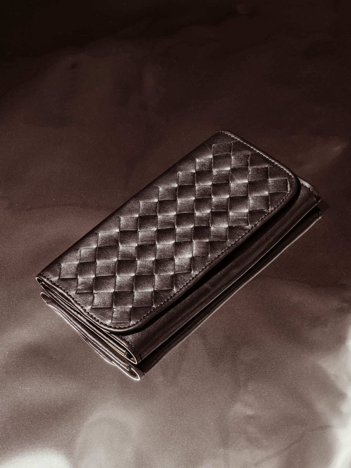 Black leather braided wallet on silver background.