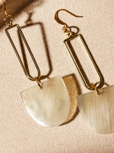 Elegant drop earrings featuring rectangular gold-plated frames and translucent horn pendants, photographed on a beige textured surface.