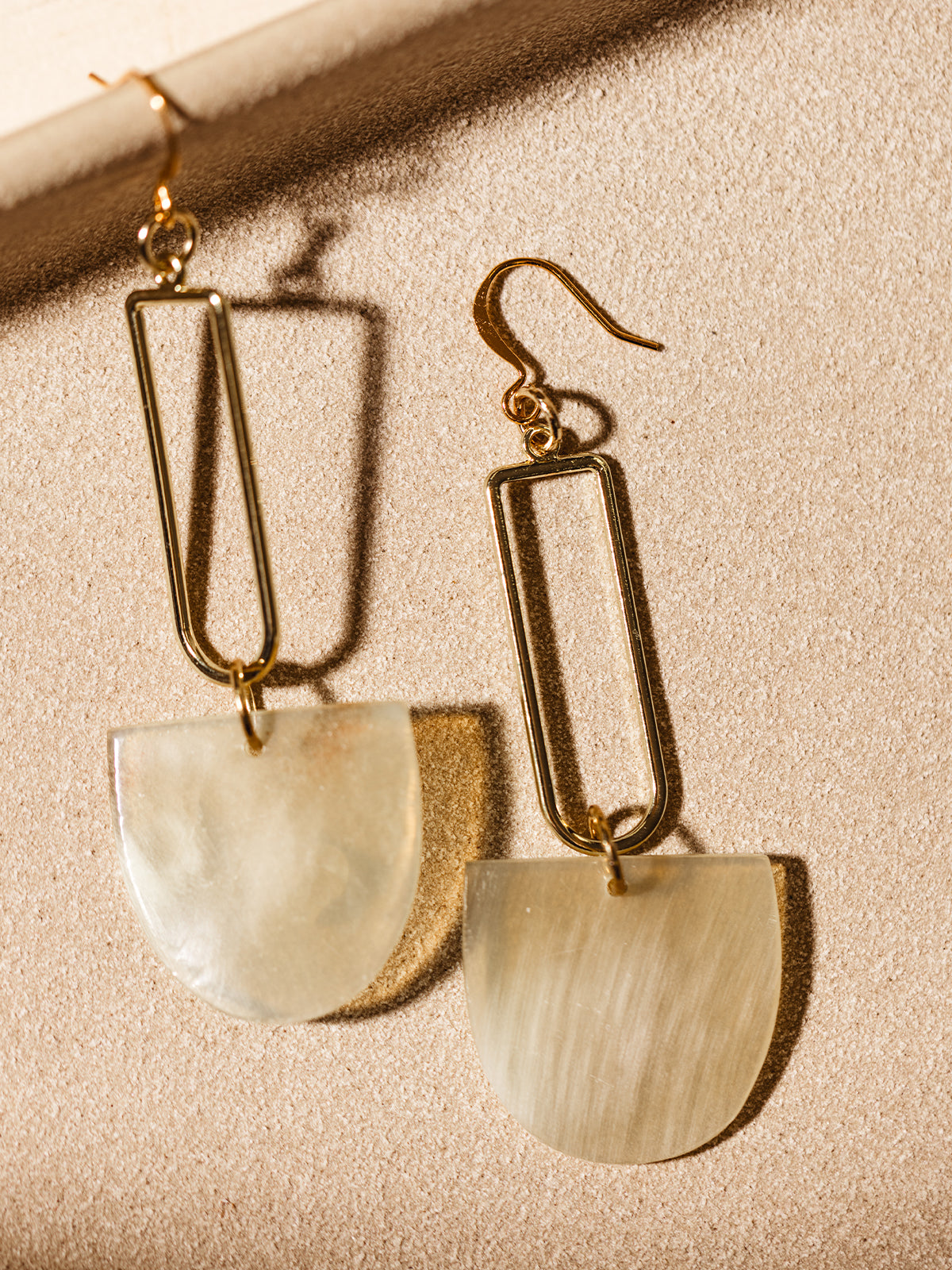 Close-up of artisanal drop earrings with gold rectangular frames and natural horn pendants, styled against a neutral backdrop.