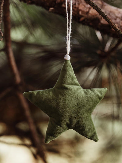 Handmade green fabric star ornament, hanging from a pine tree branch with twine, perfect for adding a rustic and cozy feel to holiday decorations.
