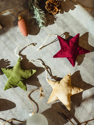 Handcrafted fabric star ornaments in red, green, and beige, placed on a festive surface with pinecones and frosted greenery.