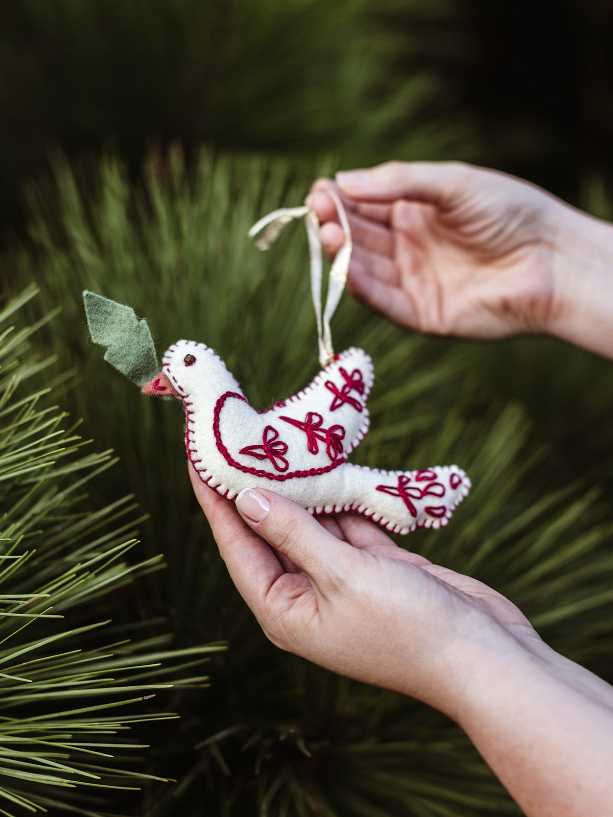 Handmade felt dove ornament with red embroidery and green leaf detail being held before hanging on Christmas tree – ethical holiday decor gif